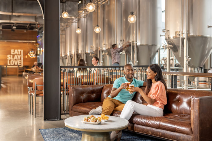 Legacy Hall Unlawful Assembly - couple enjoying beverages on a couch with food 