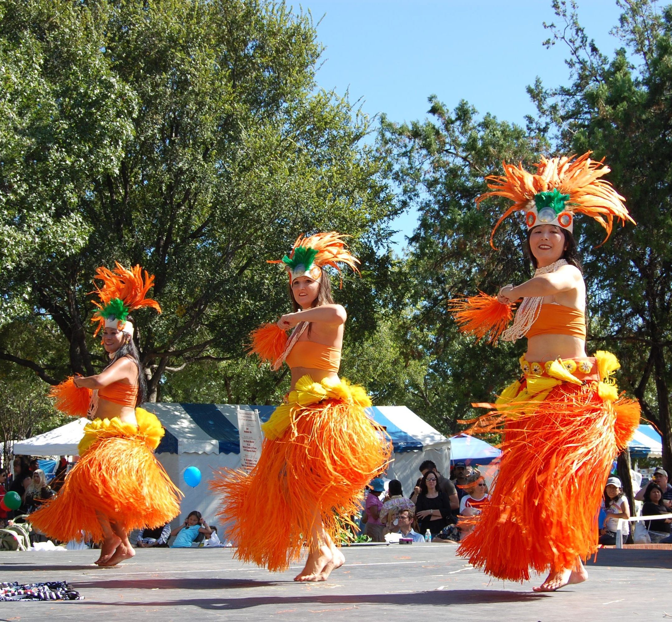 Dancers in orange grass skirts dance at Plano International Festival