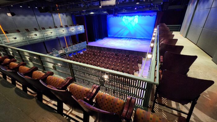 View of the Courtyard Theater from the balcony, showcasing rows of polka-dot pattern seats below, a lit stage with blue lighting, and modern design elements like metal railings.