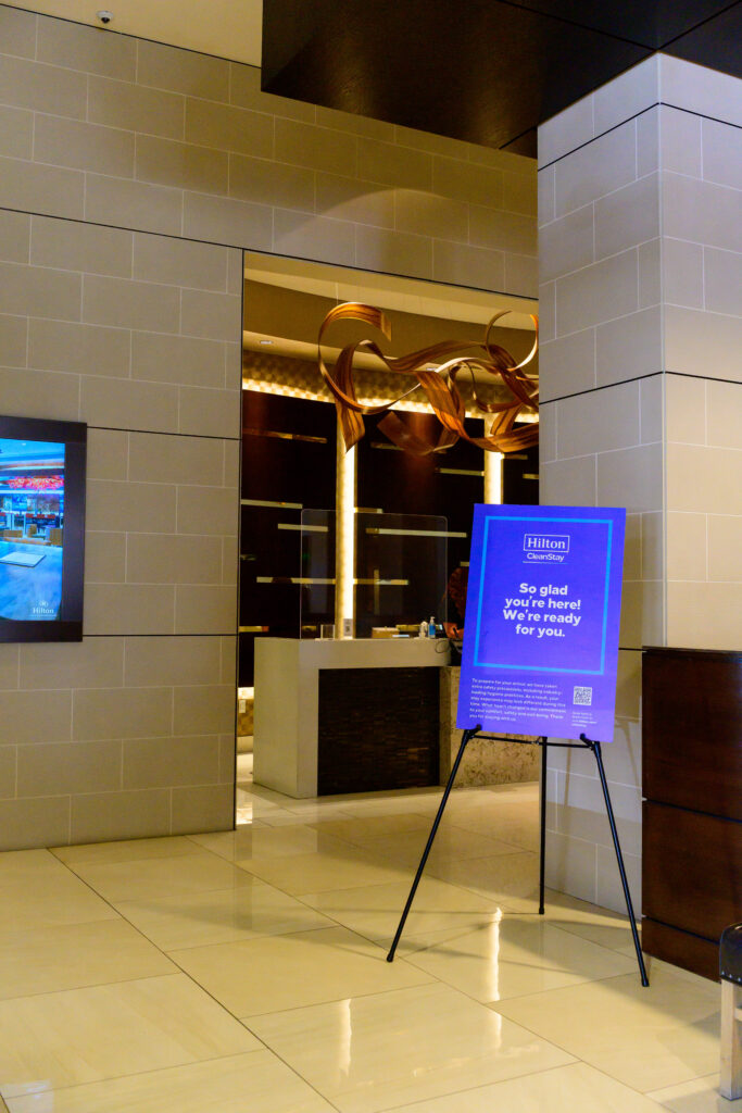 Hilton Granite Park lobby check-in counter and So lad You're Here sign.