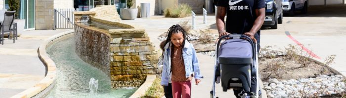 Girl, dad, and baby strolling outside of the Hilton Granite Park in Plano, TX