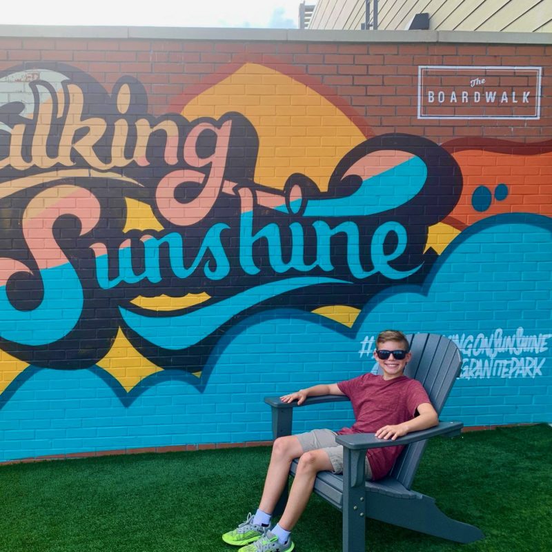 Kid posing in front of a mural at The Boardwalk at Granite Park in Plano, TX