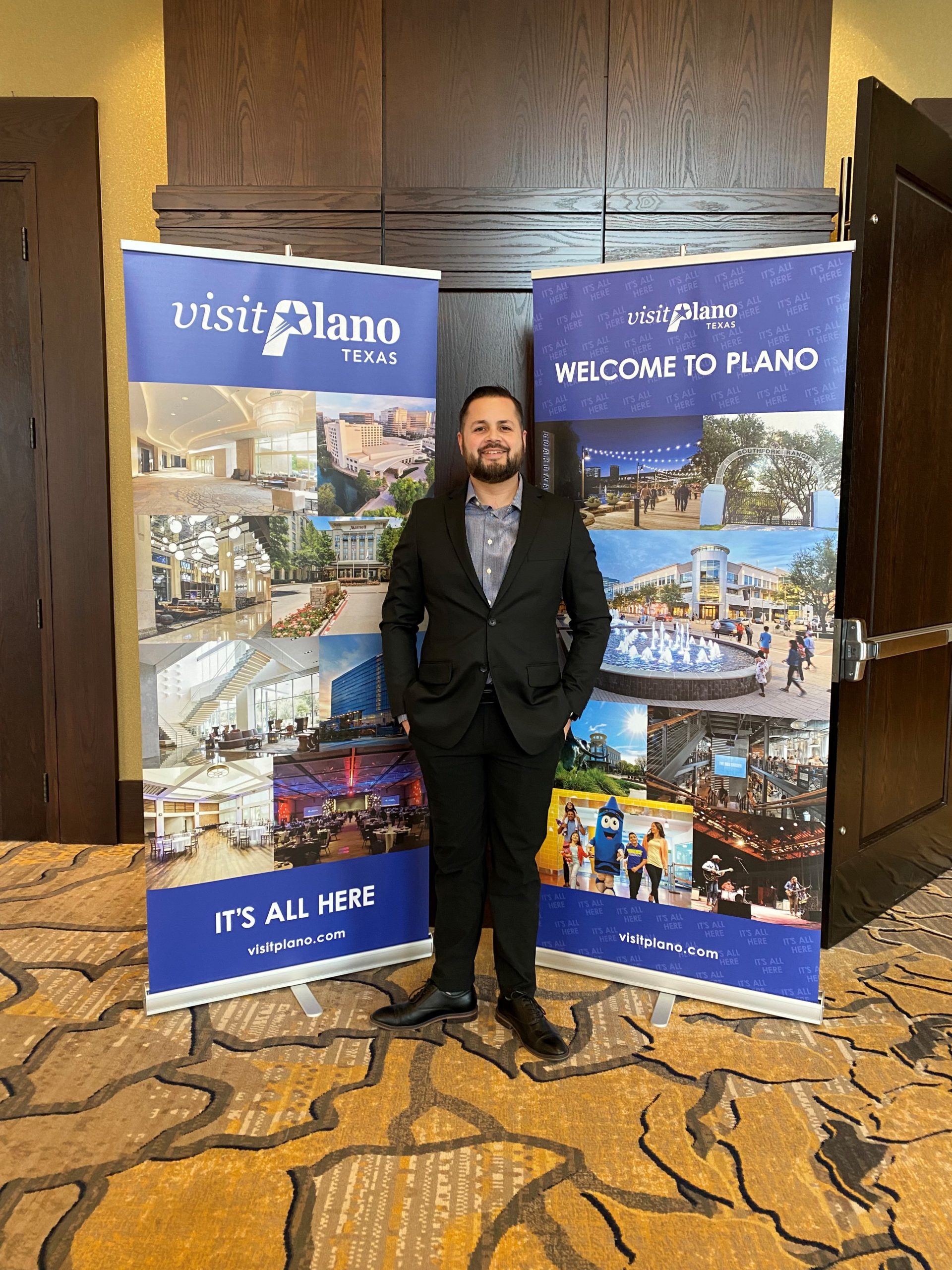 Visit Plano Sales Manager, Steven Simmons, standing in front of Visit Plano's pop-up banners.