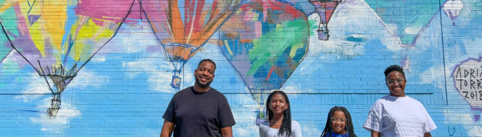 Things to Do in Plano TX by The Spring Break Family posing in front of a hot air balloon mural