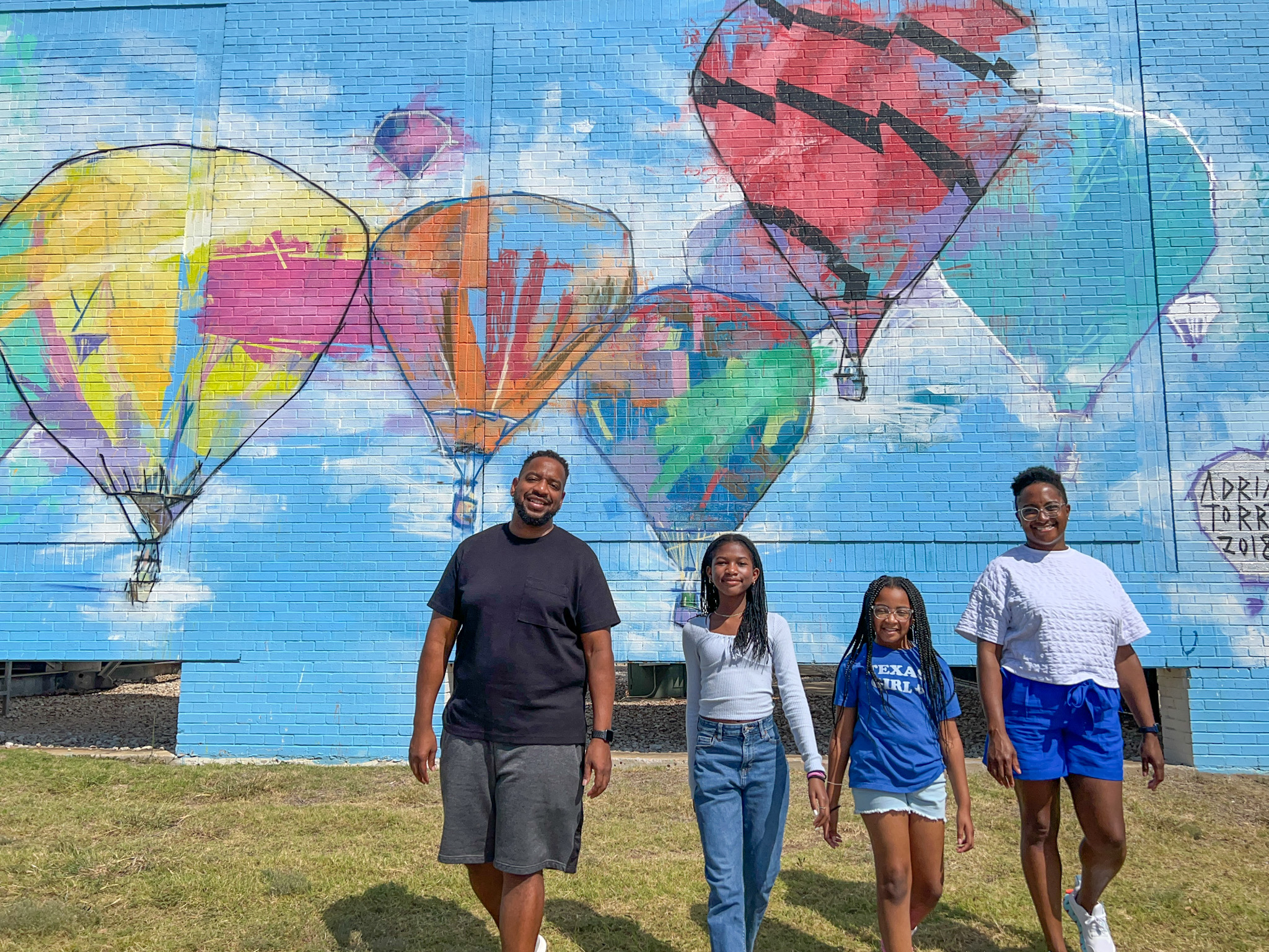 Things to Do in Plano TX by The Spring Break Family posing in front of a hot air balloon mural