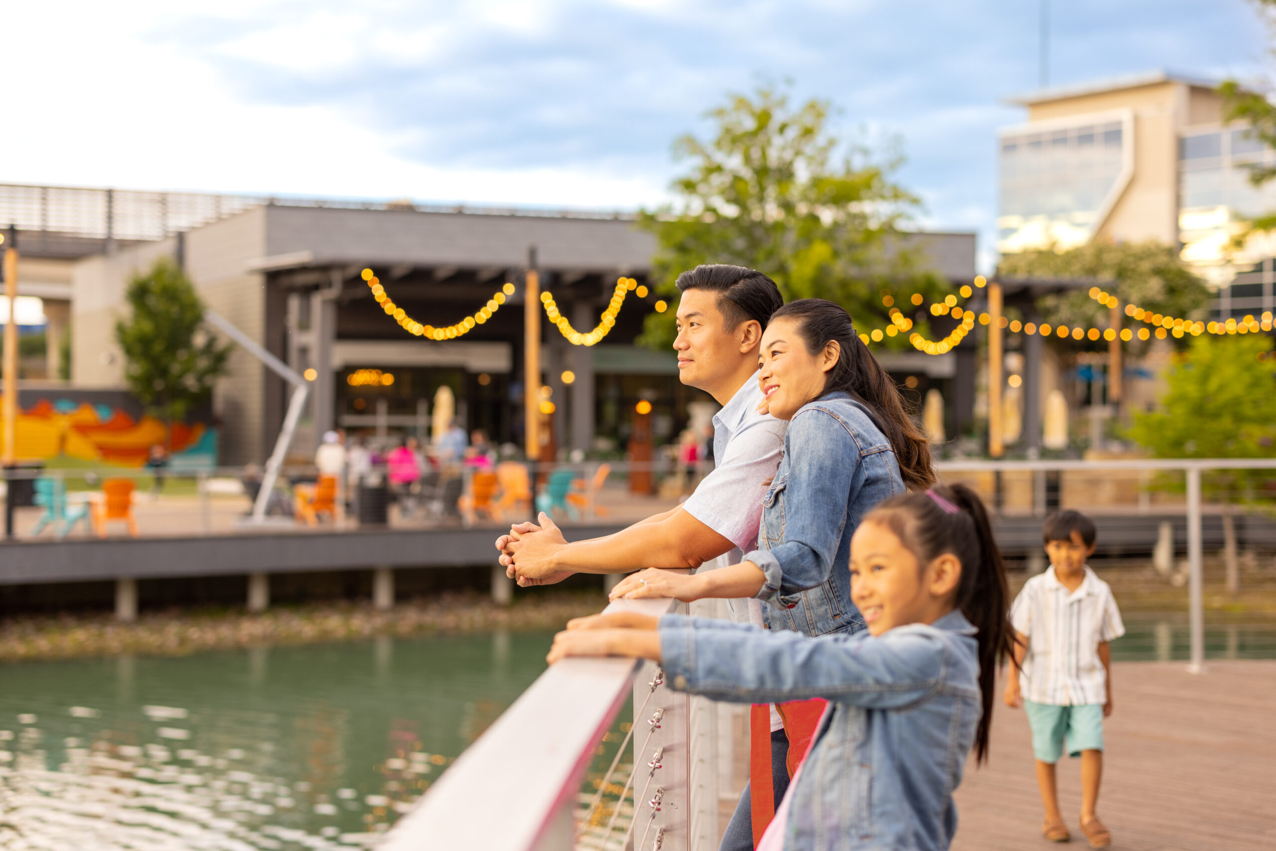 Wife hugs husband with kids running around and enjoying the Boardwalk at Granite Park in Plano for Father's Day