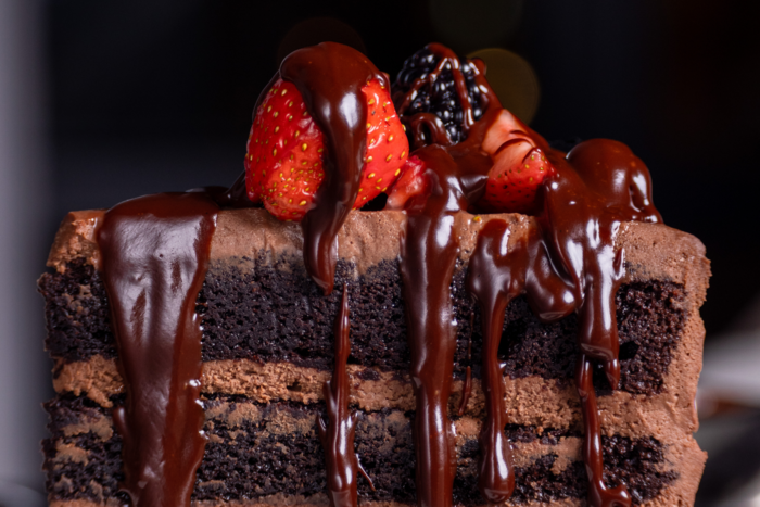 A close-up of a decadent chocolate layer cake from Truluck's, topped with fresh strawberries and blackberries and covered in glossy chocolate sauce dripping down the sides.