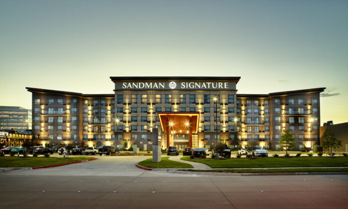 The image shows the exterior of the Sandman Signature hotel at dusk.