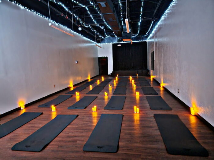 A yoga studio with rows of black mats on a wooden floor, surrounded by flameless candles and string lights along the ceiling, creating a warm, calming atmosphere at venueiztic.