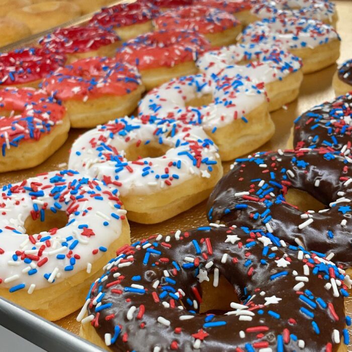 Rows of donuts topped with chocolate, white, and red icing, each covered with red, white, and blue sprinkles, are arranged neatly on a tray—perfect for a sweet Breakfast in Plano.