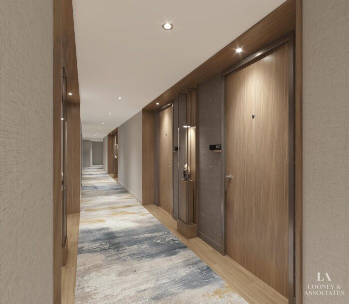 A modern hotel hallway with wooden doors, neutral walls, recessed lighting, and a patterned carpet. A small display shelf is built into the wall near one door. Looney & Associates logo is in the bottom right corner.
