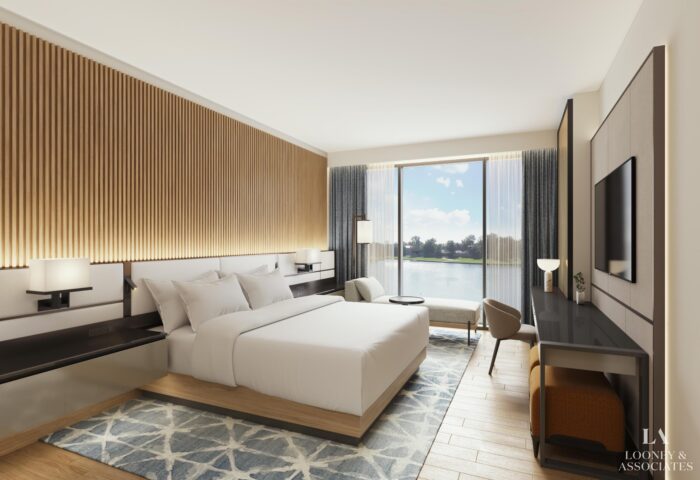 A modern hotel room with a large bed, wooden accents, a wall-mounted TV, desk, armchair, and window with a view of a lake and trees outside. Natural light brightens the neutral-toned, stylish space.