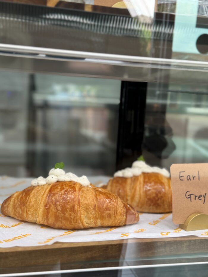Two golden croissants filled with cream and topped with white cream and small dark specks are displayed in a glass case. A label beside them reads Earl Grey.