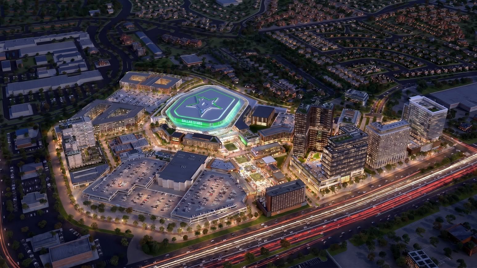 Aerial night view of a brightly lit, modern entertainment and shopping complex with parking lots, high-rise buildings, and busy highways, surrounded by residential neighborhoods.