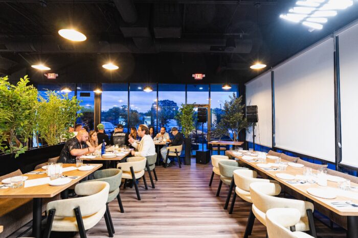 Patrons dine at tables in Olive and Fig, a modern restaurant with floor-to-ceiling windows and potted greenery.
