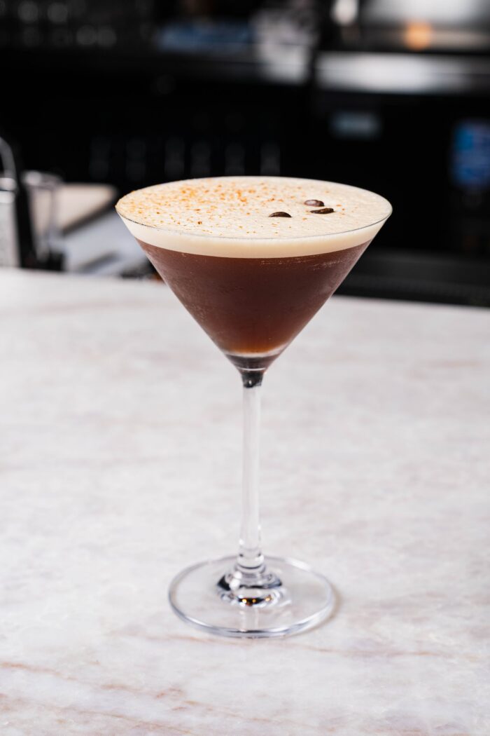 An espresso martini served at Olive and Fig in a martini glass, topped with foam and two coffee beans.