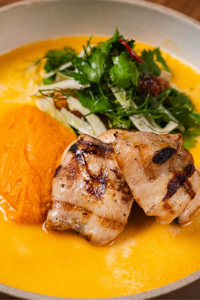 Grilled chicken with a mound of pureed olive and fig vegetables, topped with fresh herbs in a creamy yellow sauce.