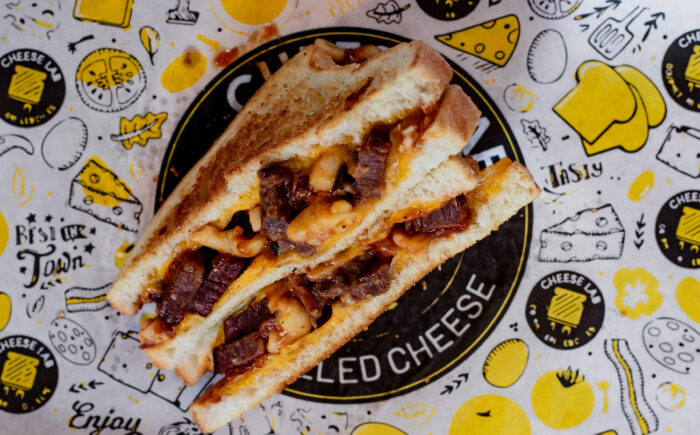 A grilled cheese sandwich with beef and melted cheese, cut in half and placed on colorful, cheese-themed paper.