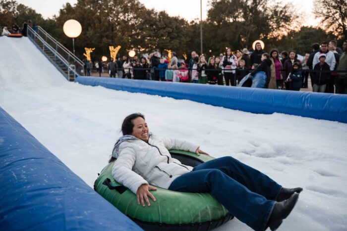 A woman laughs while sliding down an artificial snow hill in a green tube at a Holiday Event in Plano.